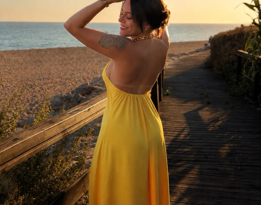 Mulher de vestido amarelo num passadiço junto à praia, ao pôr do sol